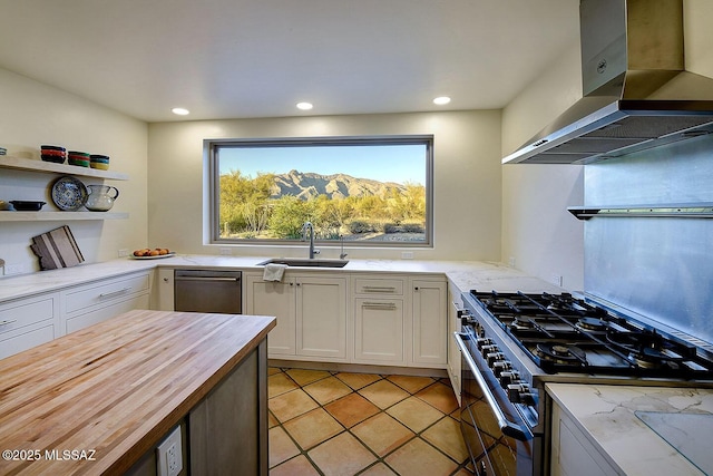 kitchen featuring a sink, appliances with stainless steel finishes, wooden counters, wall chimney range hood, and white cabinets