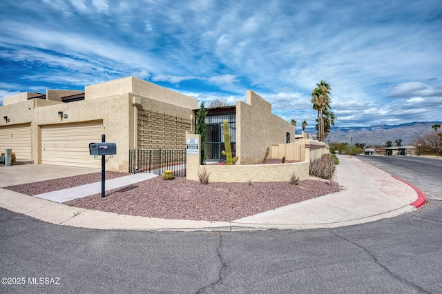 view of side of property with a fenced front yard, stucco siding, concrete driveway, an attached garage, and a mountain view