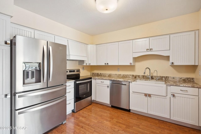 kitchen featuring white cabinets, light stone countertops, stainless steel appliances, light wood-style floors, and a sink