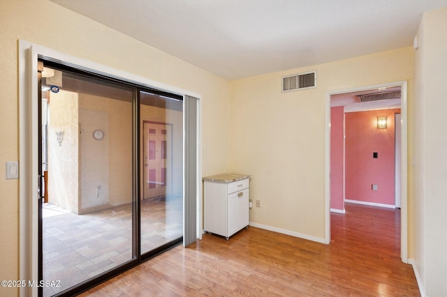 empty room with light wood-type flooring, baseboards, and visible vents