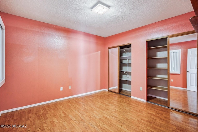 unfurnished bedroom featuring multiple closets, a textured ceiling, baseboards, and wood finished floors