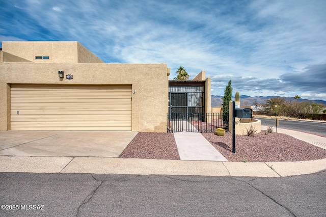 view of front of house featuring stucco siding, a gate, fence, a garage, and driveway