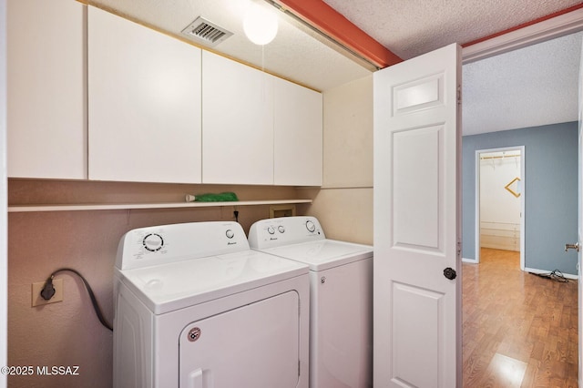 laundry room featuring a textured ceiling, separate washer and dryer, visible vents, light wood-type flooring, and cabinet space