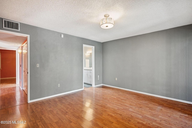 unfurnished room with visible vents, a textured ceiling, baseboards, and wood finished floors