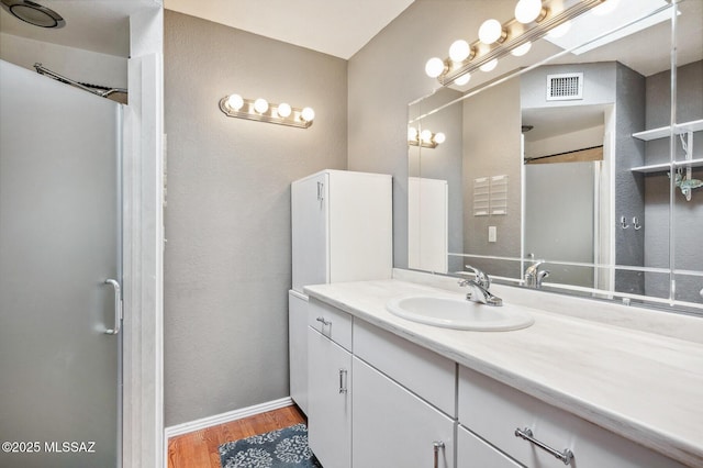 bathroom with a shower, visible vents, vanity, wood finished floors, and baseboards