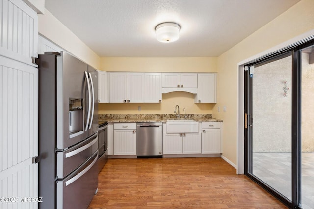 kitchen with light wood finished floors, appliances with stainless steel finishes, light stone counters, and white cabinets