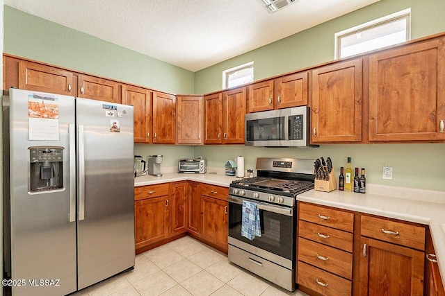 kitchen with light tile patterned floors, stainless steel appliances, light countertops, visible vents, and brown cabinetry