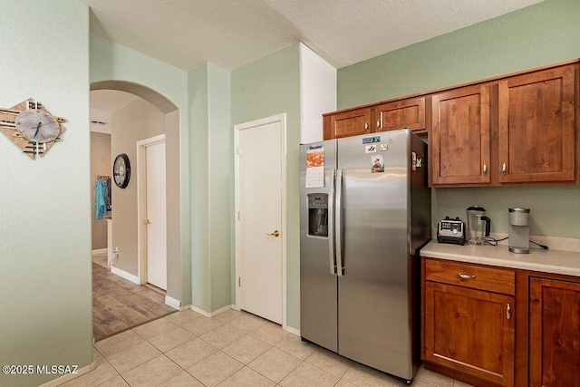 kitchen featuring arched walkways, brown cabinets, light countertops, light tile patterned flooring, and stainless steel fridge