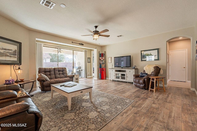 living area with arched walkways, a textured ceiling, wood finished floors, and visible vents