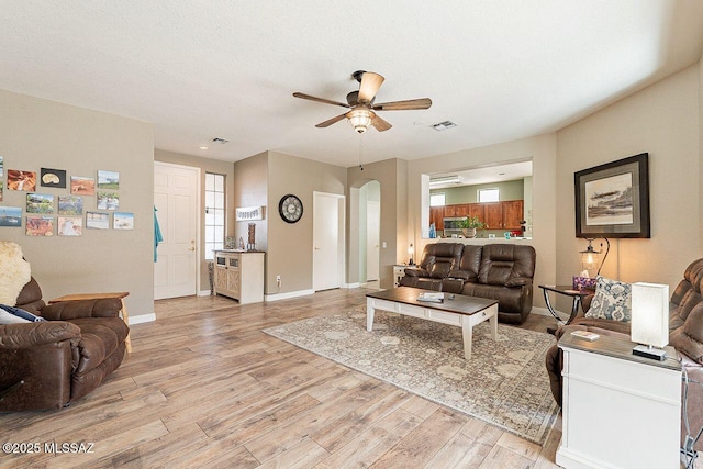 living room with arched walkways, baseboards, ceiling fan, and light wood finished floors