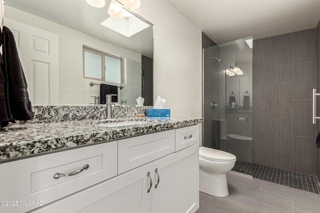 bathroom featuring a stall shower, a skylight, vanity, and toilet