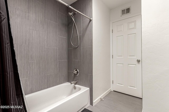 bathroom featuring shower / bathtub combination, a textured wall, visible vents, and baseboards