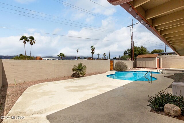 view of swimming pool with a fenced backyard, a storage unit, an outbuilding, and a patio