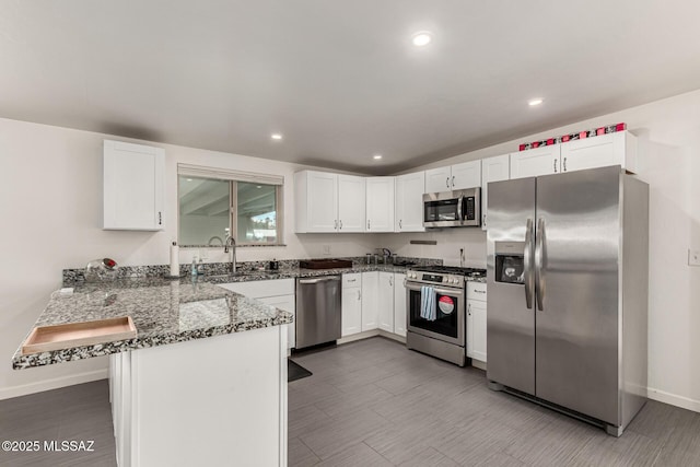 kitchen featuring appliances with stainless steel finishes, white cabinetry, a sink, dark stone counters, and a peninsula