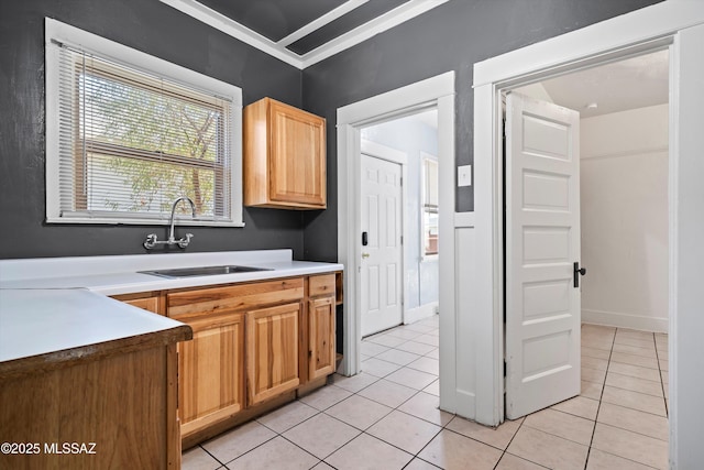 kitchen featuring baseboards, light countertops, crown molding, a sink, and light tile patterned flooring