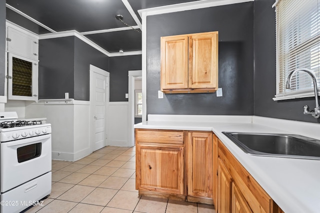 kitchen featuring light tile patterned floors, a sink, light countertops, gas range gas stove, and crown molding