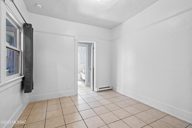 empty room with light tile patterned floors, a baseboard radiator, and baseboards