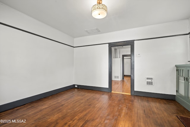 spare room with heating unit, baseboards, and hardwood / wood-style floors