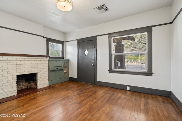 unfurnished living room featuring hardwood / wood-style flooring, a brick fireplace, visible vents, and baseboards