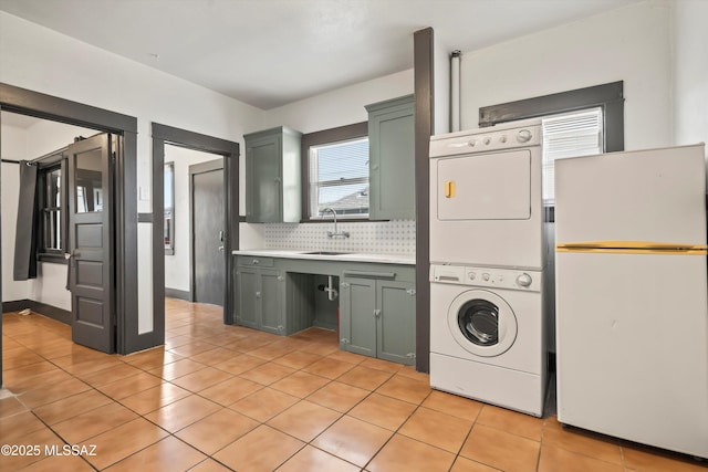 clothes washing area featuring a sink, laundry area, light tile patterned floors, and stacked washer / dryer