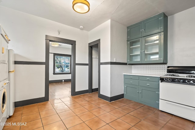 kitchen with white range with gas stovetop, stacked washer and dryer, light countertops, backsplash, and green cabinetry