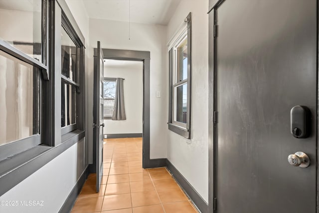 corridor featuring light tile patterned floors, attic access, and baseboards