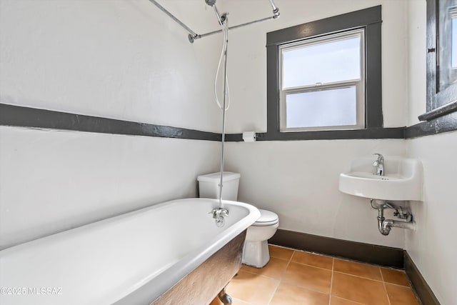 bathroom with tile patterned flooring, baseboards, a freestanding bath, and toilet