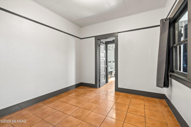 tiled empty room with baseboards and crown molding