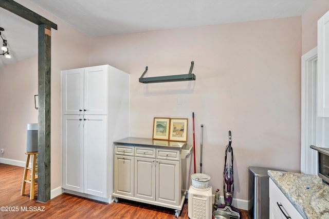 kitchen featuring dark wood finished floors, light stone counters, white cabinetry, and baseboards