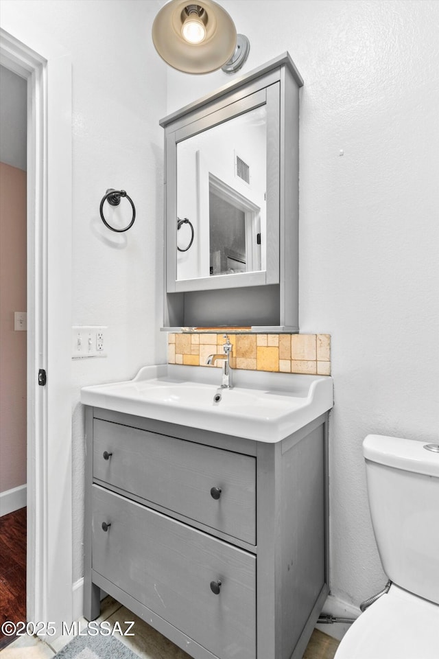 half bathroom featuring vanity, visible vents, baseboards, toilet, and tasteful backsplash