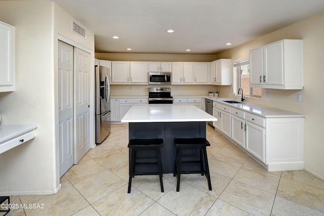 kitchen with a sink, visible vents, white cabinets, appliances with stainless steel finishes, and a center island