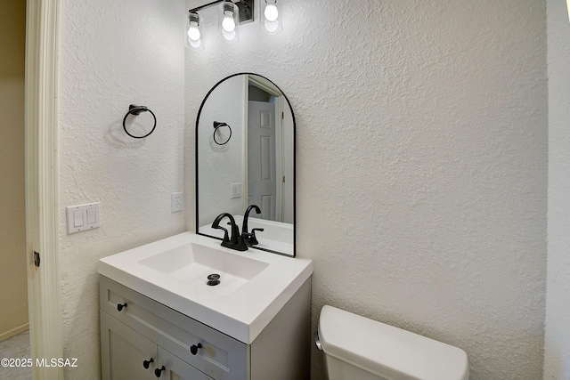 half bath featuring toilet, vanity, and a textured wall