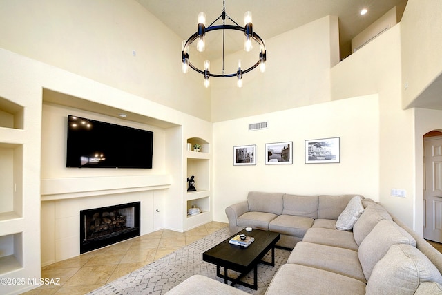 living room featuring a chandelier, built in shelves, visible vents, tile patterned floors, and a tiled fireplace