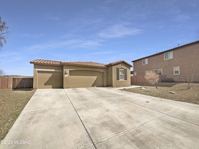 mediterranean / spanish house featuring a garage, a tile roof, fence, concrete driveway, and stucco siding