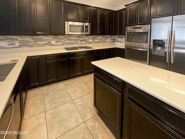 kitchen featuring light tile patterned flooring, a sink, appliances with stainless steel finishes, backsplash, and light stone countertops