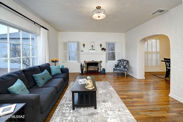 living room with visible vents, arched walkways, a textured wall, a fireplace with flush hearth, and wood finished floors