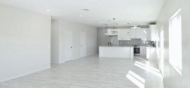 kitchen with decorative backsplash, a kitchen island, open floor plan, stainless steel appliances, and white cabinetry