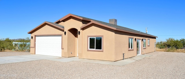 view of front of home featuring driveway, a garage, a chimney, and stucco siding