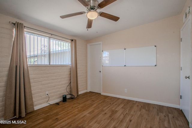 empty room featuring ceiling fan, brick wall, wood finished floors, and baseboards