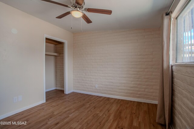 unfurnished bedroom with brick wall, wood finished floors, and baseboards