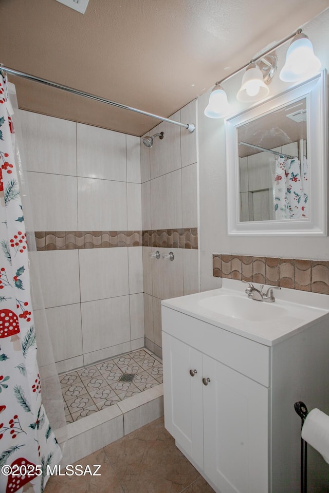 bathroom featuring tile patterned flooring, a tile shower, and vanity