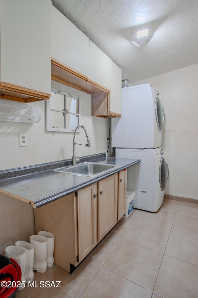 kitchen featuring light tile patterned floors, dark countertops, stacked washer / drying machine, light brown cabinetry, and a sink