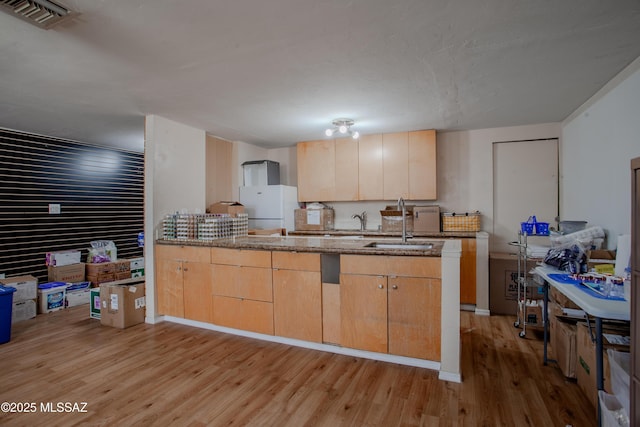 kitchen with light wood finished floors, visible vents, a peninsula, stone counters, and a sink