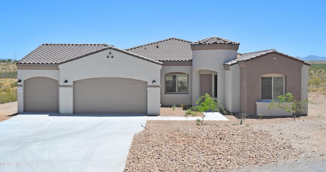 mediterranean / spanish-style house featuring an attached garage, a tile roof, concrete driveway, and stucco siding