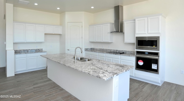 kitchen featuring light wood-style flooring, appliances with stainless steel finishes, white cabinetry, a sink, and wall chimney exhaust hood