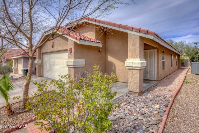 view of side of home featuring central AC unit, stucco siding, an attached garage, and a tile roof