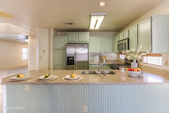 kitchen featuring a sink, light stone counters, a peninsula, appliances with stainless steel finishes, and green cabinets