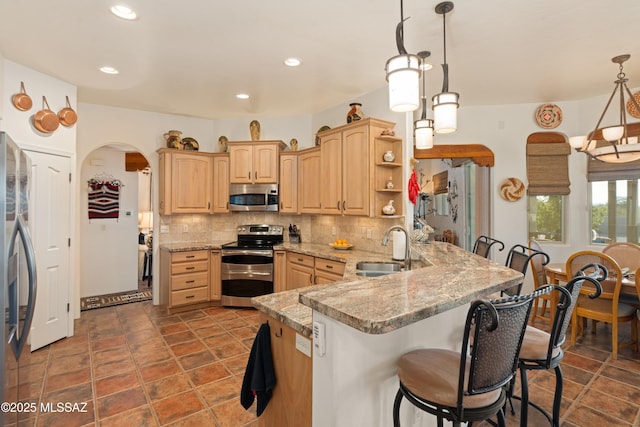 kitchen with light brown cabinets, a sink, tasteful backsplash, stainless steel appliances, and arched walkways