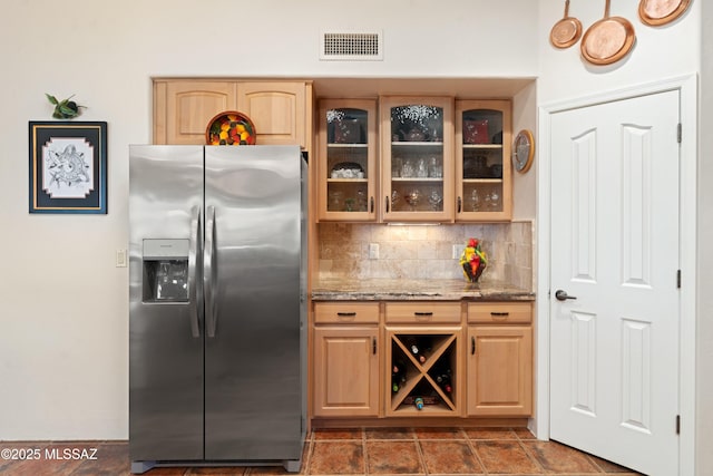 kitchen featuring tasteful backsplash, visible vents, glass insert cabinets, light stone countertops, and stainless steel fridge