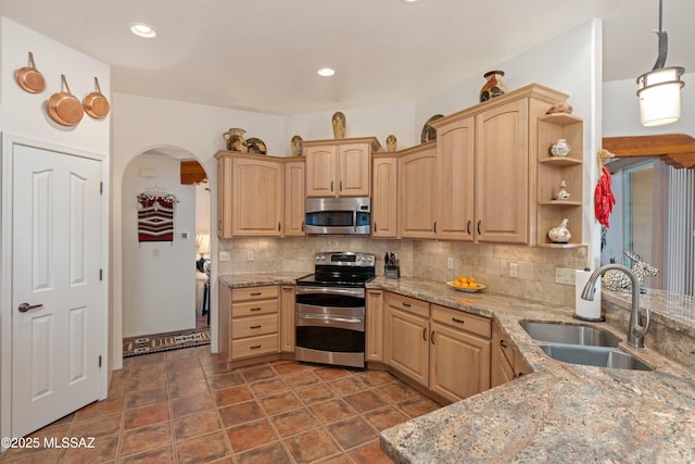 kitchen with light brown cabinets, arched walkways, a sink, decorative backsplash, and appliances with stainless steel finishes